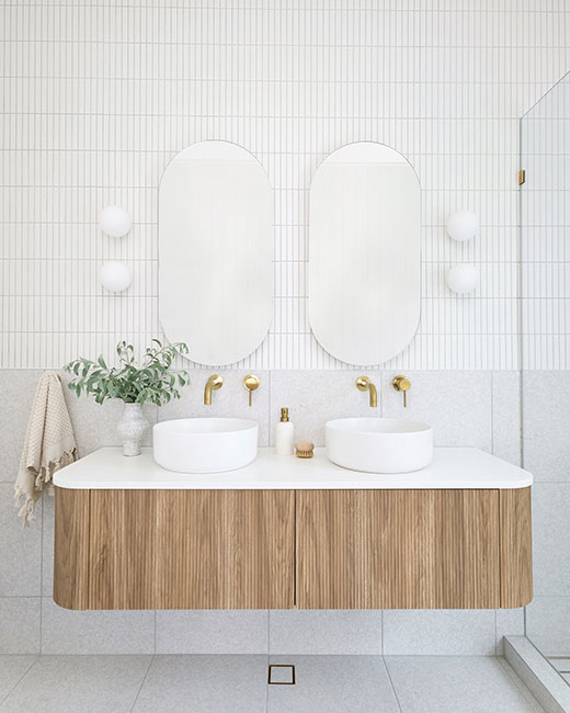A floating wooden double vanity decorated by 2 oblong mirrors in white bathroom evoking a calm ambiance.