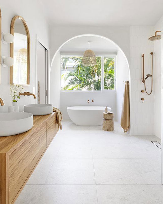 Une spacieuse salle de bains blanche avec une fusion d'accessoires en bois clair. Elle présente un concept d'espace ouvert où les formes rondes dominent